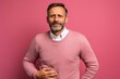 © Leon Waltz - Medium shot portrait photography of a man in his 40s holding his stomach with discomfort from gastritis wearing a chic cardigan against a pastel or soft colors background