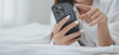 © ARMMY PICCA - Happy young female in casual clothes smiling and looking at camera while using laptop on bed in bedroom at home