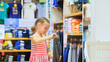 Cute shopaholic little child choose looking for clothes in clothing store.Cheerful baby shopper customer is looking and buying casual clothes in clothing store.Child choosing stylish clothes in store