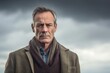 © Leon Waltz - Medium shot portrait photography of a man in his 50s with a somber and deeply sad expression due to major depression wearing a chic cardigan against a sky and clouds background