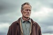 © Leon Waltz - Medium shot portrait photography of a man in his 50s with a somber and deeply sad expression due to major depression wearing a chic cardigan against a sky and clouds background