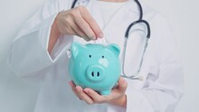 Doctor Holding Piggy Bank And Putting Coin. And Healthcare Cost, Money Saving, Health Insurance, Medical, Donation And Financial Concepts