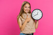 © Andrii Iemelianenko - It is your time. Young attractive woman showing time on wall office clock, ok, thumb up, nice good, approve, start, pointing finger at camera. Blonde girl isolated on pink studio background, indoors
