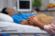 © WESTOCK - Close up shot of wife hands or family hands praying for admitted fathers health recovery at hospital near bed - concept of family caring, Emotional Bonding and togetherness