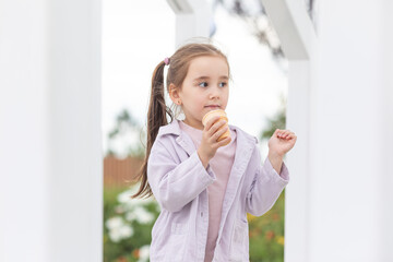 Wall Mural - A hungry child enjoys eating ice cream outdoors. Portrait of a cute baby licking a creamy ice cream while walking in a city park, outdoor activities.