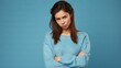 Hesitant and worried young woman frowning pointing fingers up with sad face standing on blue background