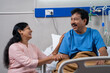 © WESTOCK - Happy smiling Indian wife talking with recovered husband near bed at hospital ward - concept of successful medial treatment, family bonding and Joyful Conversation