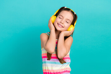 Wall Mural - Photo of lovely peaceful small girl closed eyes arms touch headphones favorite song isolated on teal color background