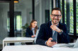 © bnenin - Portrait of a businessman with glasses on sitting at the office, holding a mobile phone.