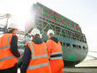 © Connect Images - Managers communicating by dockside infront of cargo ship and cranes