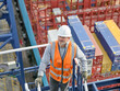 © Connect Images - Looking down on dock worder supervisor going down railings with container ship and cargo in background