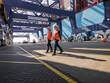 © Connect Images - Two dock workers walking under steel structure in dockyard, Felixstowe, England.