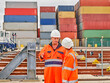 © Connect Images - Dock workers in protective workwear discussing with cargo containers in background, Felixstowe, England.