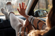 Graceful female sitting on co-driver seat inside modern car, putting legs on dashboard