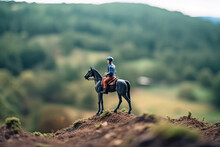 Miniature Figurine Of Rider With Hat Sitting On Horse Stands On Edge Of Cliff In Mountains Looking Into The Distance