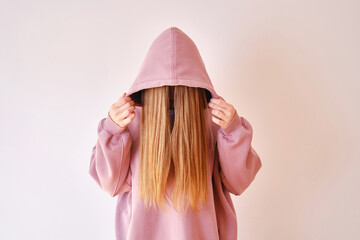 Wall Mural - Young beautiful girl in a pink hoodie posing. Warm oversized hoodie with an hood. Stylish trendy hipster bow. Trying on clothes in a store. Youth subculture. Fashion clothing advertising