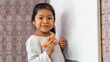 © JAHF - Niña latina sonriente y feliz, escribiendo en la pizarra de clases con plumones de colores. Espacio para texto.