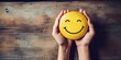 World Mental Health Day. Hands holding a happy smile, round yellow ball, on a wooden background, relax face, good feedback rating, think positively. Place for text.