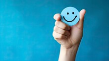 World Mental Health Day. Hand Holding Blue Cut Paper Happy Smiling Face On Blue Background. Space For Copy Text.