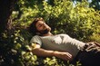 © Tuyres - A fictional young man sleeping in the grass under a tree in a garden. Generative AI.