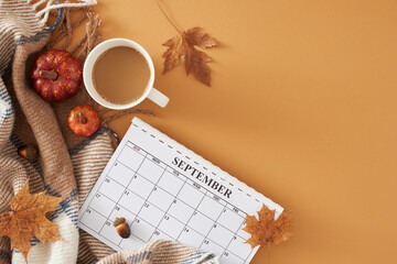 Get cozy with autumn decor in september. Top view photo of calendar, cocoa mug, warm blanket, pumpkins, acorns, dry maple leaves on pastel brown background with empty space for promo or text