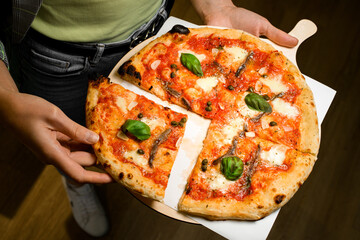 Restaraunt worker hold in hands wooden tray with fresh delicious Italian pizza and separates one slice