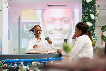 Wall Mural - Smiling african american cashier scanning customer clothes at cash register. Woman standing at counter desk, waiting to pay for purchase while employee using pos terminal and scanner