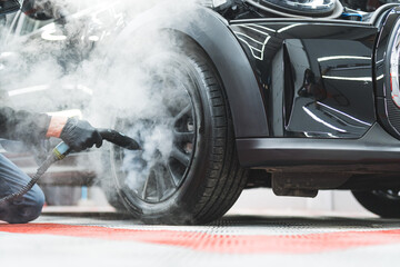 professional mechanic with black gloves cleaning a car tire with steam at the workshop. High quality photo