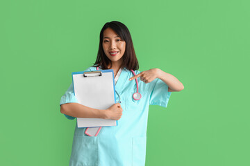 Sticker - Female Asian medical intern pointing at clipboard on green background