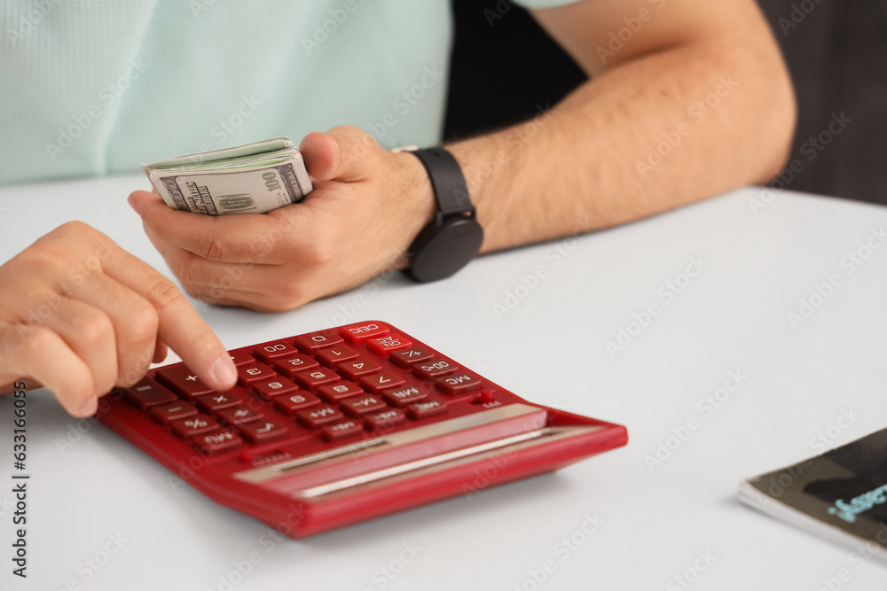 Young man counting money with calculator in kitchen, closeup
