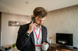 © Miljan Živković - one man adult caucasian businessman wear suit in hotel room while taking a brake or prepare for work hold cup of coffee and smartphone making a phone call talk real people copy space