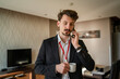 © Miljan Živković - one man adult caucasian businessman wear suit in hotel room while taking a brake or prepare for work hold cup of coffee and smartphone making a phone call talk real people copy space