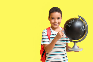 Sticker - Little African-American boy with school backpack pointing at globe on yellow background