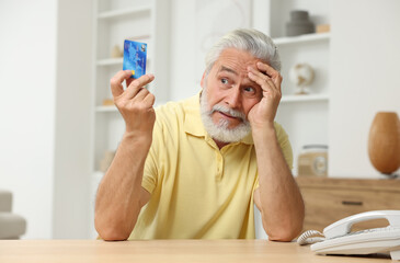 Canvas Print - Confused senior man with credit card at home. Be careful - fraud