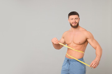 Wall Mural - Portrait of happy athletic man measuring waist with tape on light grey background, space for text. Weight loss concept