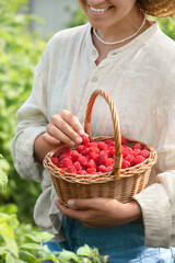 Canvas Print - Woman holding wicker basket with ripe raspberries outdoors, closeup