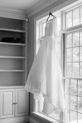 Wall Mural - Bride's wedding dress hung up against a large window in black and white