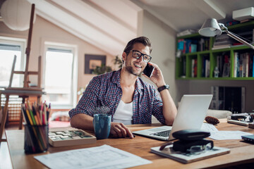 Young man talking on his smart phone while working from home on his laptop