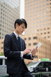 © monzenmachi - オフィス街でタブレットを見るビジネスマン