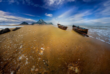 Lonely Wooden Fishing Boats On The Beach With Sky And Majestic Mountains In The Distance Before Sunset