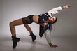 © Alexander - female street dancer with a sporty figure in black shorts, jacket and black boots posing in the studio on a gray background