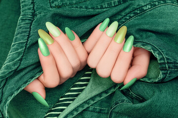 Female hands with glitter nail polish. Green nail design with two shades. Women hands with sparkle manicure on green denim background.