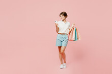 Full Body Young Smiling Woman Wear Casual Clothes Hold Shopping Paper Package Bags Hold In Hand Use Mobile Cell Phone Isolated On Plain Pink Color Background Studio. Black Friday Sale Buy Day Concept.
