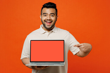 Young surprised IT Indian man wears white t-shirt casual clothes hold use work point on laptop pc computer with blank screen workspace area isolated on plain orange red background. Lifestyle concept.