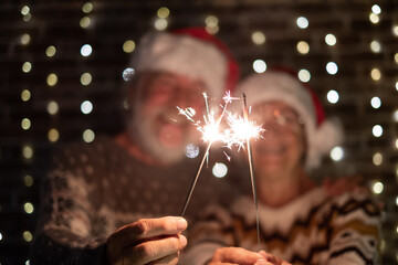 Wall Mural - Blurred senior couple in Santa hat celebrate together with love and romance new year event night firing sparklers. Man and woman enjoy magic moment relationship at Christmas time