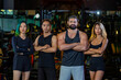 © Akarawut - Group portrait of diversity muscular gym trainers standing cross hand together inside gym with dark tone background for exercise and workout concept