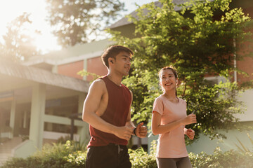 Two Asian young athlete man and woman in sportswear jogging exercise in park outdoor. Together young couple running outdoor under sunshine in the morning. Healthy exercise concept.