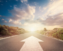 Success Concept On An Open Road With White Arrow At Sunset Sky Clouds