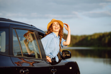 Wall Mural - Happy traveler woman in a hat having fun and enjoying the sunset from the car window. Freedom, rest, relax. Car travel