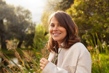 Happy smiling woman with brown hair walking in summer park outdoor